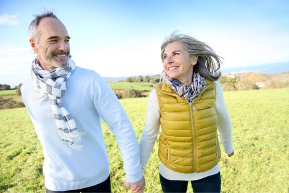 An older couple holding hands on a walk through a field